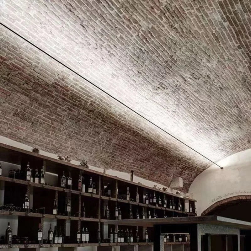 A Stream of Light Suspension Light transforming a heritage brick wine cellar with its sleek linear silhouette and warm directional glow, curated by Domus Collective.