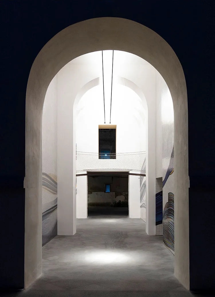 Suspended A Stream of Light fixture bringing architectural elegance to a minimalist arched entryway with soft ambient illumination, Domus Collective Design Masterpieces.