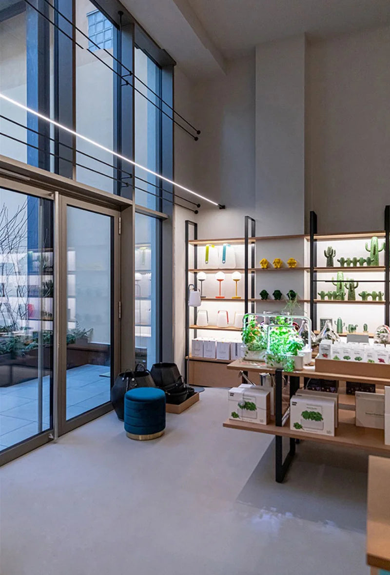 Domus Collective A Stream of Light Suspension Light spanning a double-height retail interior with its distinctive linear form creating sophisticated ambient glow.