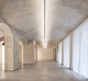 A Stream of Light Suspension Light with minimalist linear form creating soft ambient illumination beneath a sculptural vaulted concrete ceiling, Domus Collective architectural lighting.