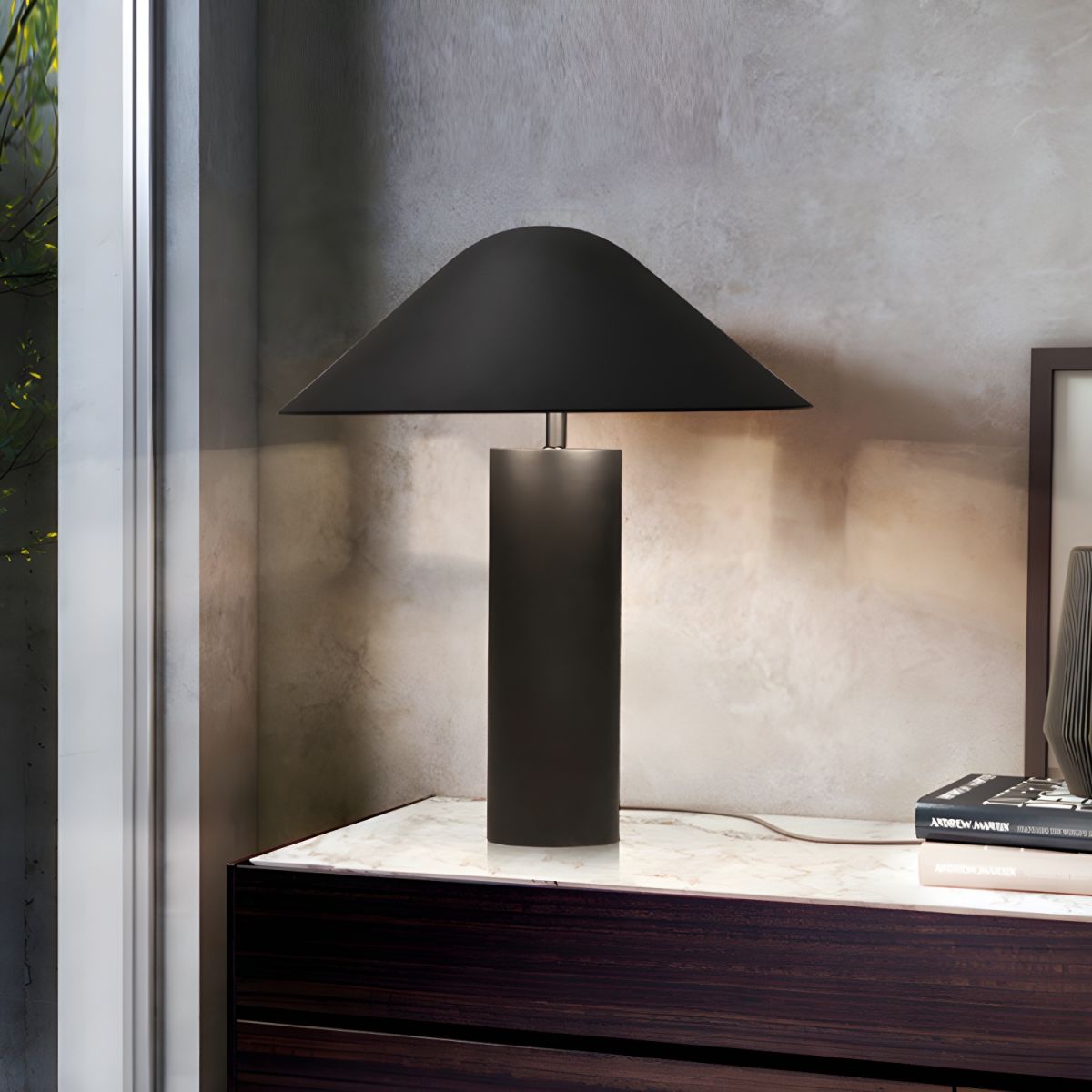 Contemporary table lighting featuring symmetrical mushroom shade and cylindrical base in sophisticated charcoal aluminum, the Asymetra Table Lamp complements textured concrete walls and marble surfaces.