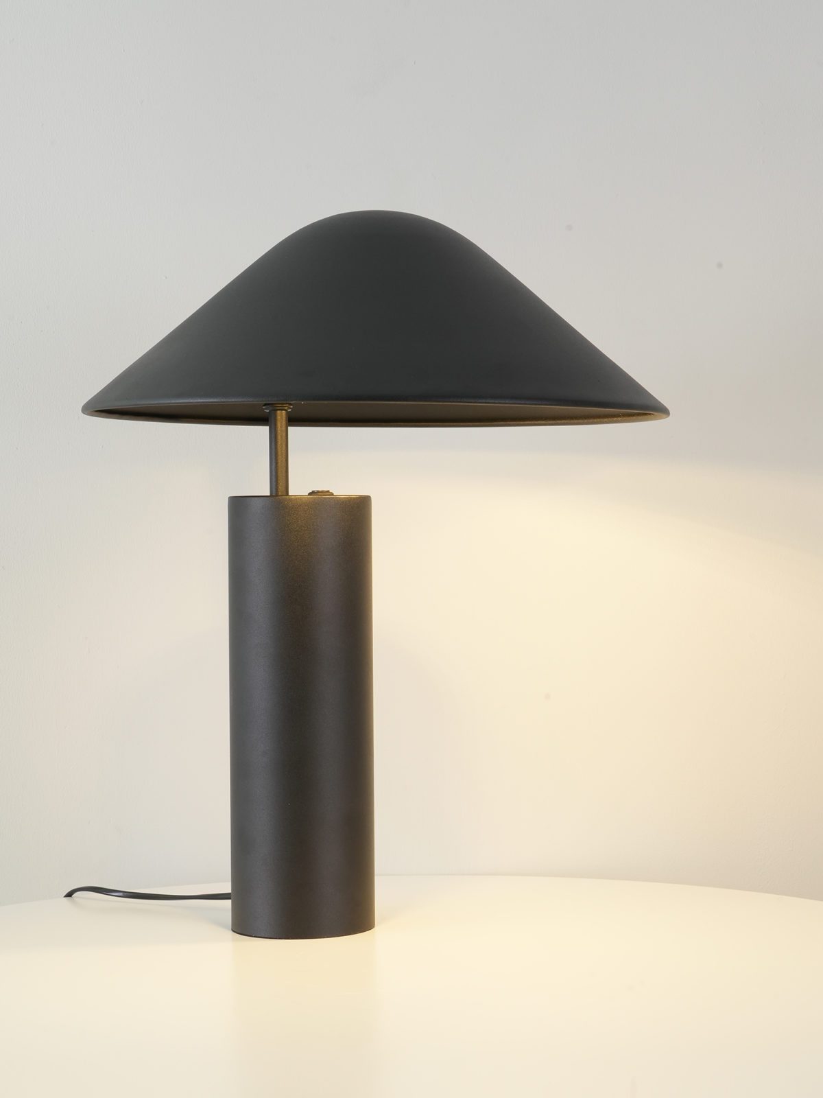 Full profile of the Asymetra Table Lamp showcasing the balanced proportions of its wide conical shade and sturdy cylindrical base in matte charcoal with brass stem detail by Domus Collective.