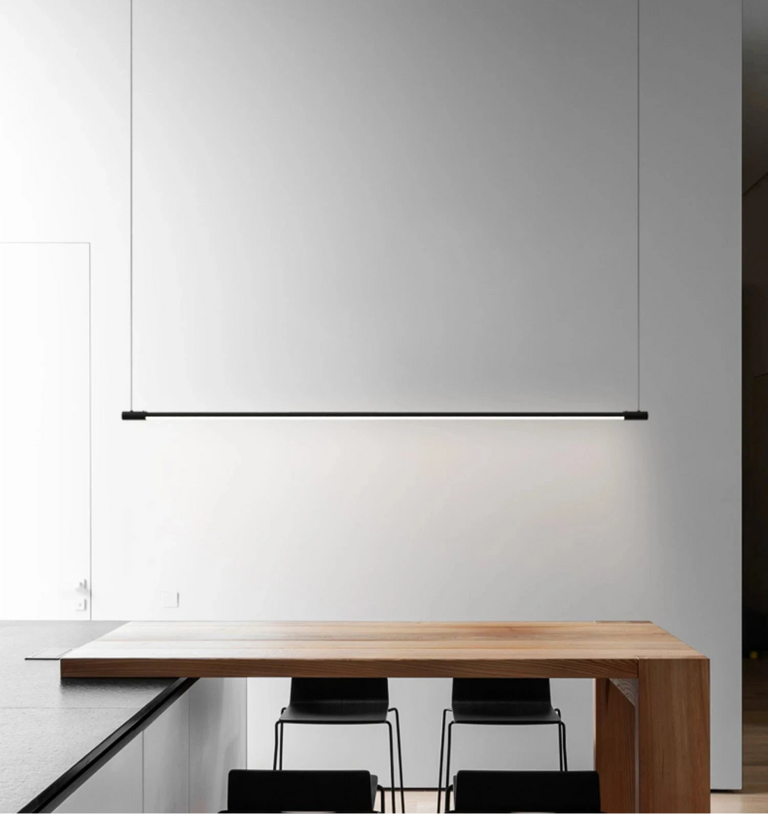 Clean, considered and architecturally refined -the Black Axiom Pendant Light in a slender linear form hovering above a warm oak dining table, bringing soft ambient glow to a minimalist contemporary interior by Domus Collective.