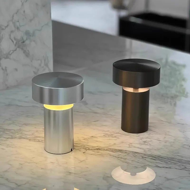 Two Cologne Halo Night Portable Lights in brushed silver and brown finishes displayed on a marble countertop, their soft halo illumination perfect for modern kitchen or bar settings, by Domus Collective.
