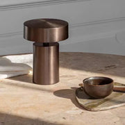 Elegant Cologne Halo Night Portable Light in brushed bronze iron finish on a travertine table beside artisan ceramics, its sculptural cylindrical form bringing understated sophistication to contemporary interiors.