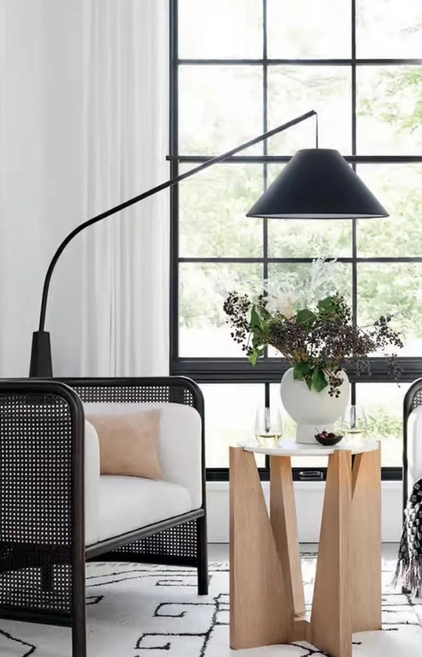 Minimalist Driftwood Reel Floor Lamp in black beside rattan armchair with conical shade creating focused ambient glow, from Domus Collective curated floor lamp collection for modern living spaces.
