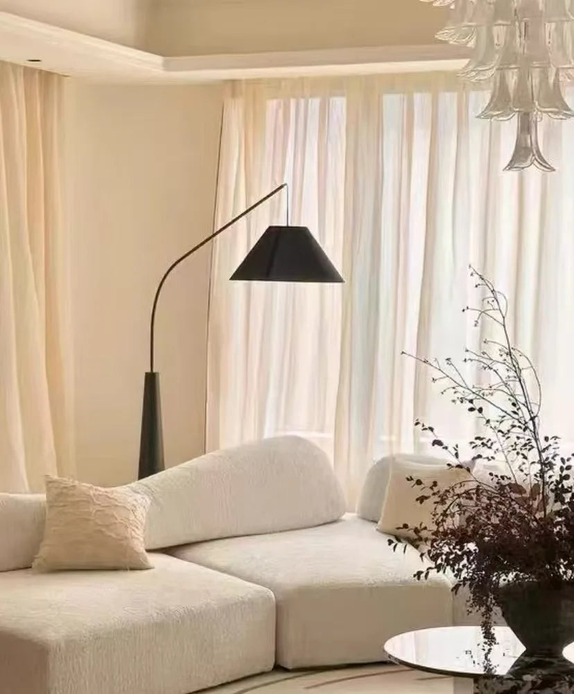 Driftwood Reel Floor Lamp in black with matching conical shade arching over white boucle seating in cream-toned living room,a Domus Collective sculptural floor lighting creating serene ambient warmth.
