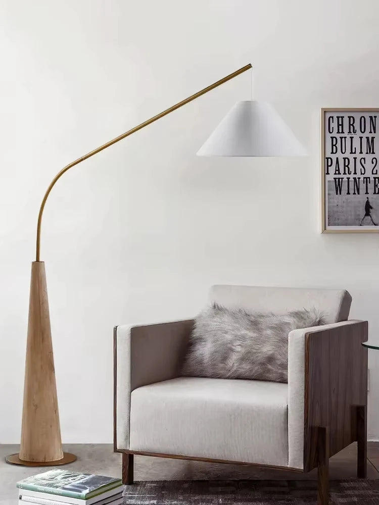 Contemporary Driftwood Reel Floor Lamp with blonde base and brass arm supporting white cone shade beside modern armchair, Domus Collective organic craftsmanship for characterful Australian homes.