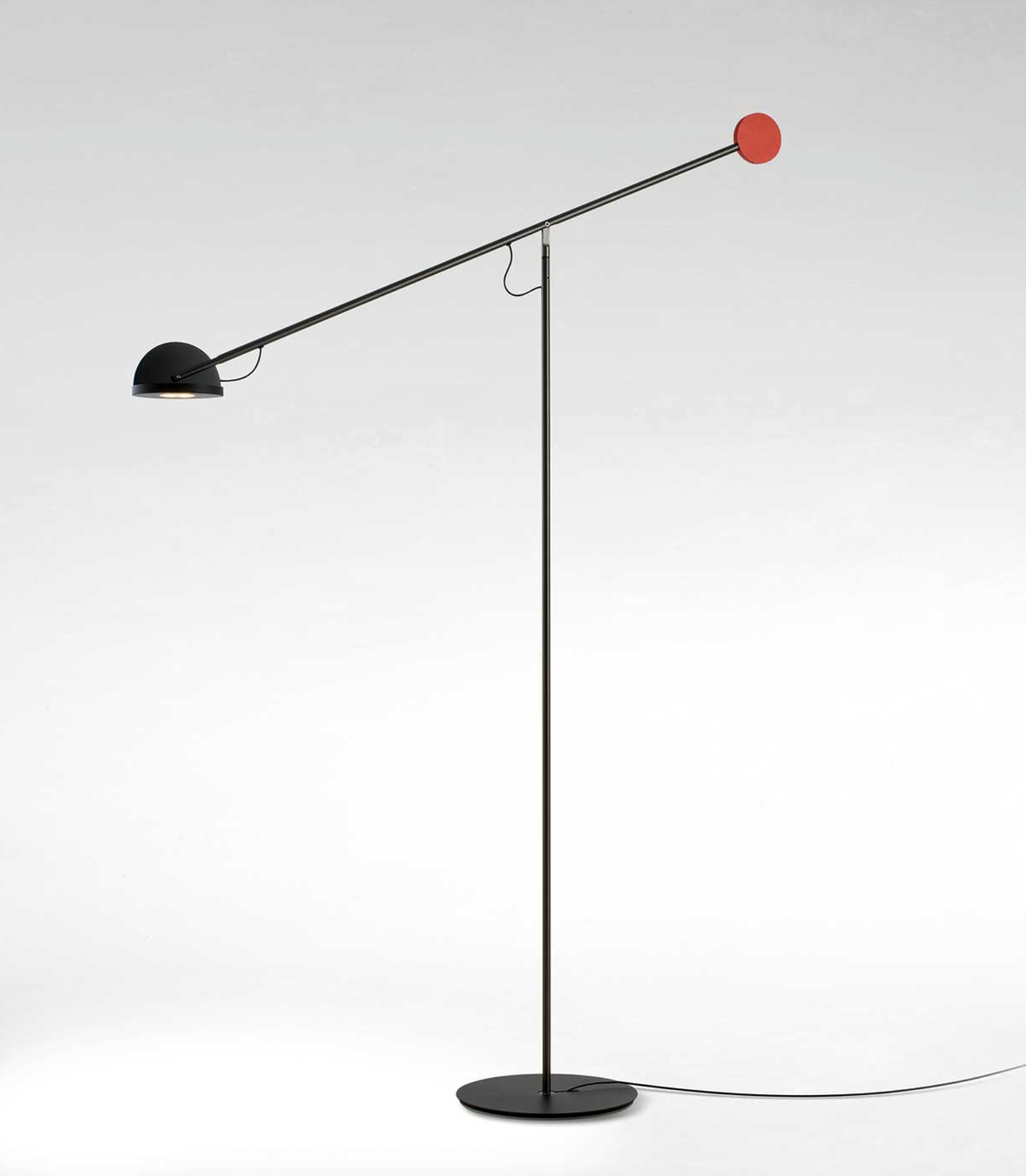Arched plaster walls and patterned tile floors frame this Dynamic Equilibrium Floor Lamp with red sphere counterweight, its tilted arm casting focused reading light over a linen sofa in a Mediterranean-inspired living room, by Domus Collective.