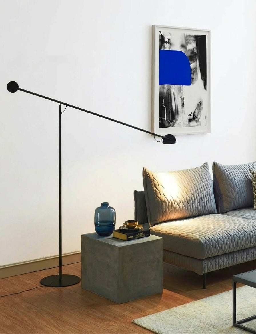 The Dynamic Equilibrium Floor Lamp with red accent counterweight complements warm concrete textures and natural light in this minimalist architectural interior, demonstrating refined balance between function and sculpture, by Domus Collective.