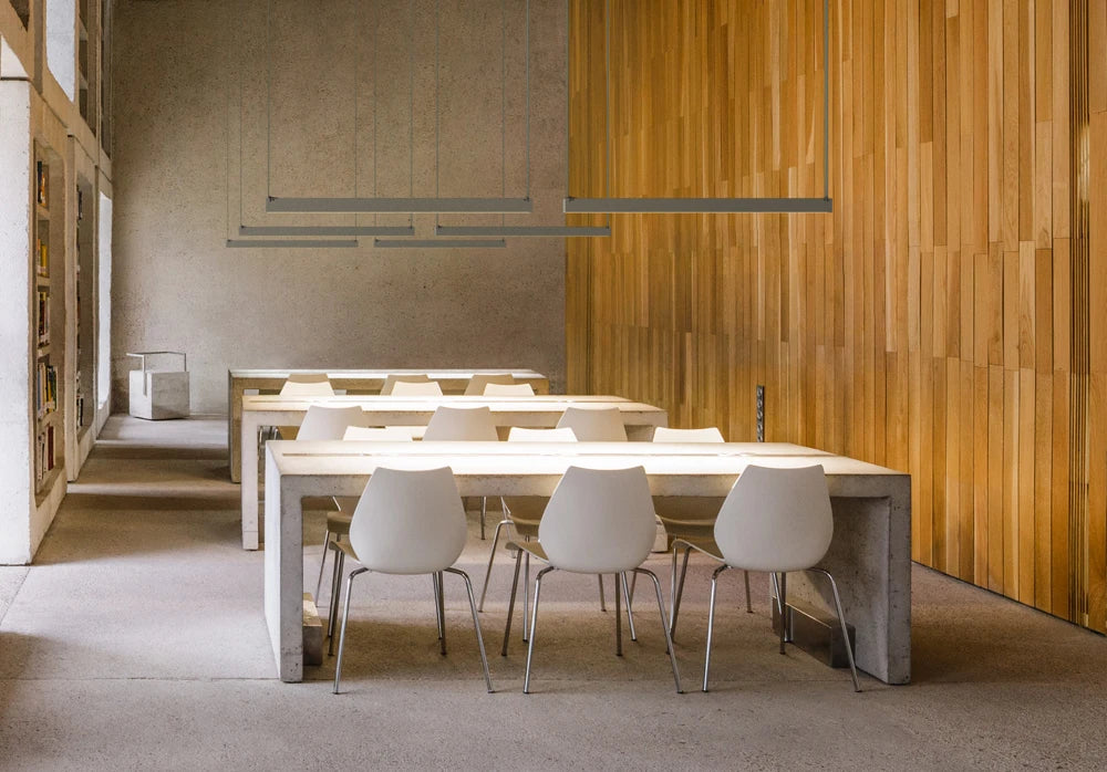 EmDash Suspension Lights in polished grey steel, their clean linear silhouettes floating above raw concrete and warm timber surfaces -a masterclass in layered architectural lighting for characterful, contemporary dining and workspace interiors by Domus Collective.