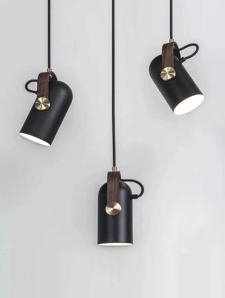 Film Projector Pendant Light cluster showcasing adjustable matte black cylinders with brushed brass knobs and walnut suspension straps, industrial-modern fixtures for creative workspaces, by Domus Collective.