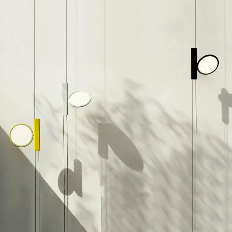 Trio of suspended  Suspension Lights in yellow, white, and black finishes casting ethereal shadows on a sunlit wall, sculptural lighting by Domus Collective.