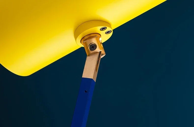 Close-up of Flyaway Floor Lamp brass pivot mechanism connecting yellow shade to blue arm,by Domus Collective refined hardware detail showcasing the sculptural craftsmanship within modern lighting.
