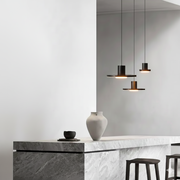Galaxia Suspension Lights cluster featuring volcanic stone disc shades with matte black metal cylinders, suspended at staggered heights above a sculptural marble kitchen island by Domus Collective.