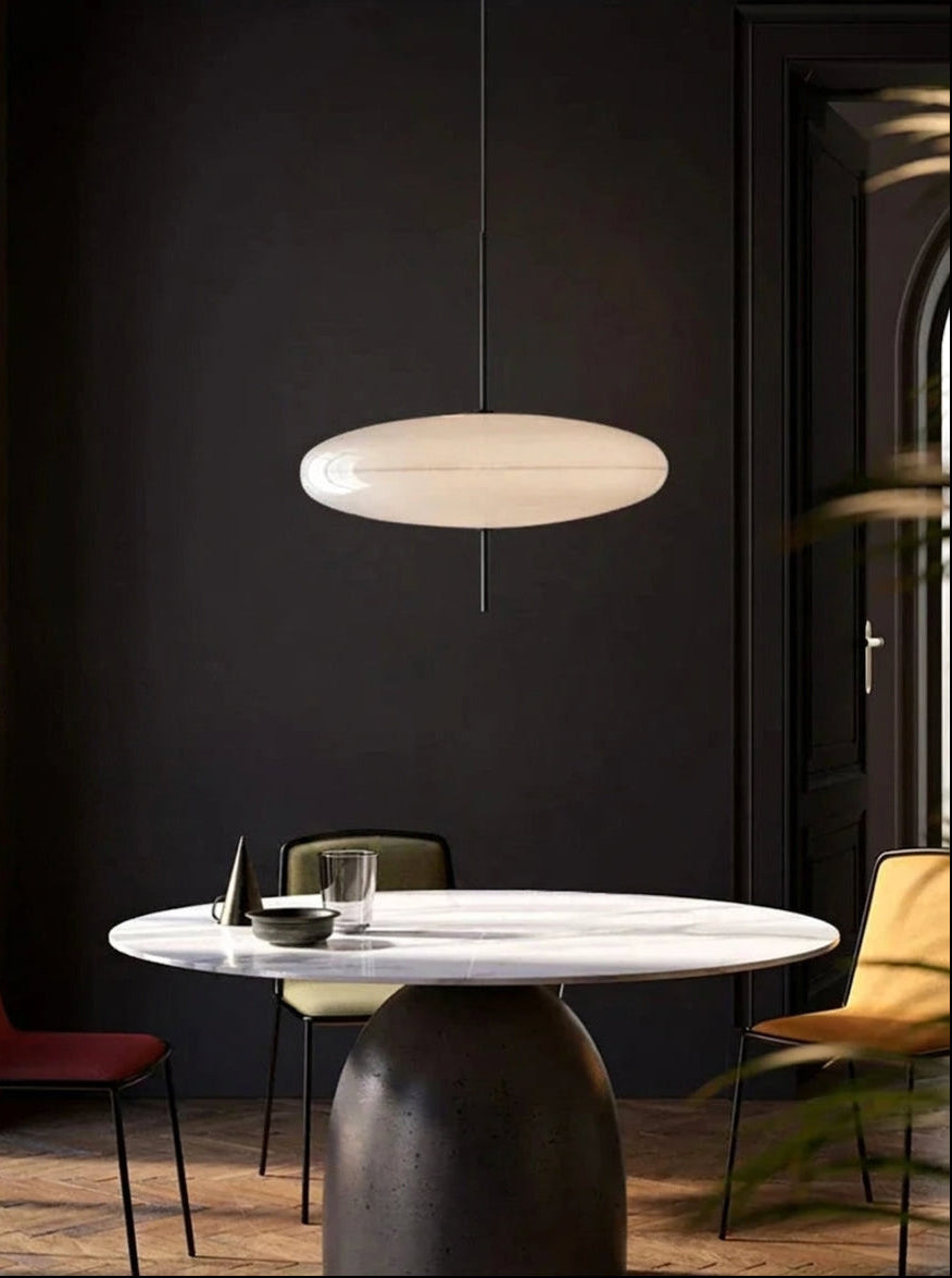 Modern dining area with a marble round table and a white Hovering Cloud Pendant Light pendant light by Domus Collective against a dark wall.
