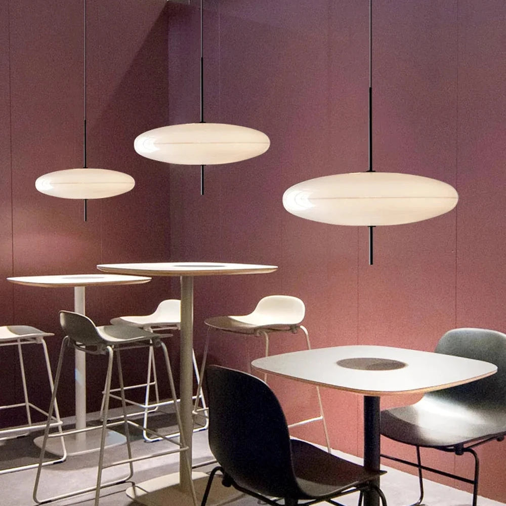 Minimalistic interior with 3 Hovering Cloud Pendant Lights in white by Domus Collective in the forefront, tables, and chairs against a restaurant's pink wall.