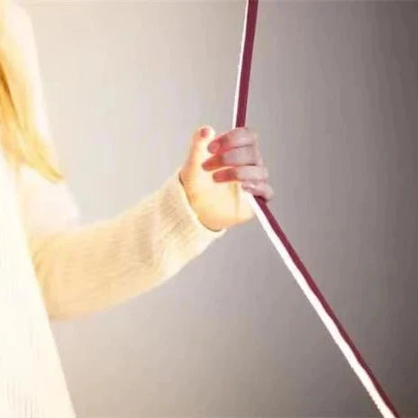 Close-up of the flexible Illuminus Threads Suspension Light being adjusted by hand, demonstrating the bendable fabric-wrapped LED tube that enables creative positioning and artistic expression.