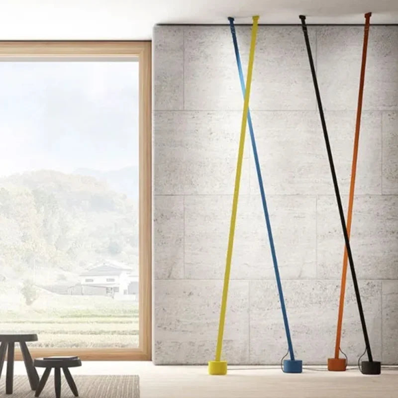 Four Illuminus Threads Suspension Lights in yellow, blue, black, and orange leaning at dramatic angles against concrete walls, their minimalist linear forms bringing bold color to Japanese-inspired interiors, by Domus Collective.