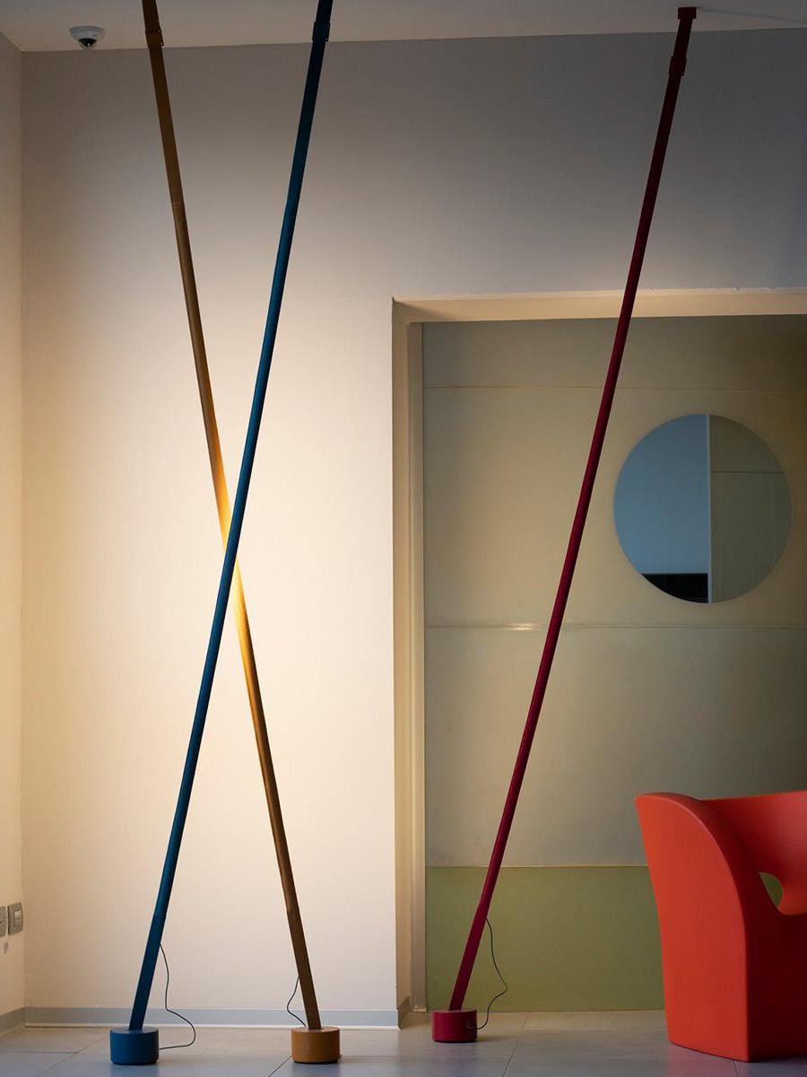 Illuminus Threads Suspension Light in teal, mustard, and burgundy crossing diagonally in a colorful contemporary space, their slender illuminated forms creating dynamic visual rhythm, by Domus Collective.