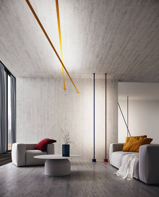 Illuminus Threads Suspension Light in yellow, navy, and red spanning from ceiling to floor in a contemporary concrete-walled living space, their slender illuminated lines creating artistic geometric drama, by Domus Collective.