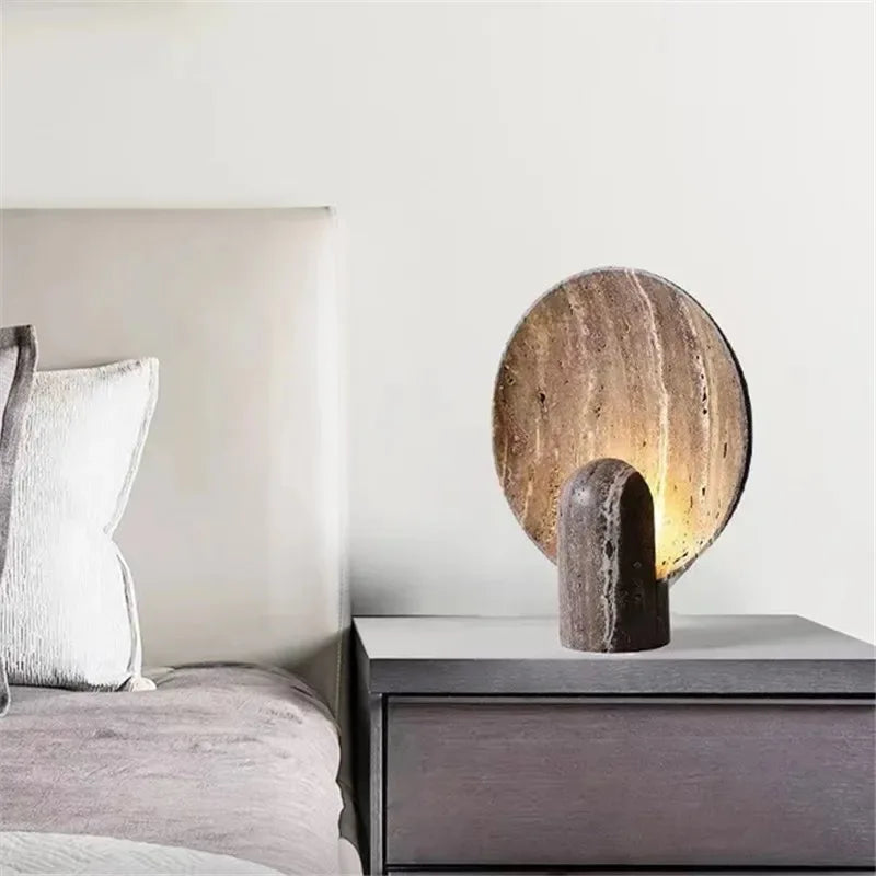 Bedside elegance with the Jupiter Halo Table Lamp, carved travertine stone featuring natural striations and porous texture with warm internal illumination for serene bedroom atmospheres, by Domus Collective.