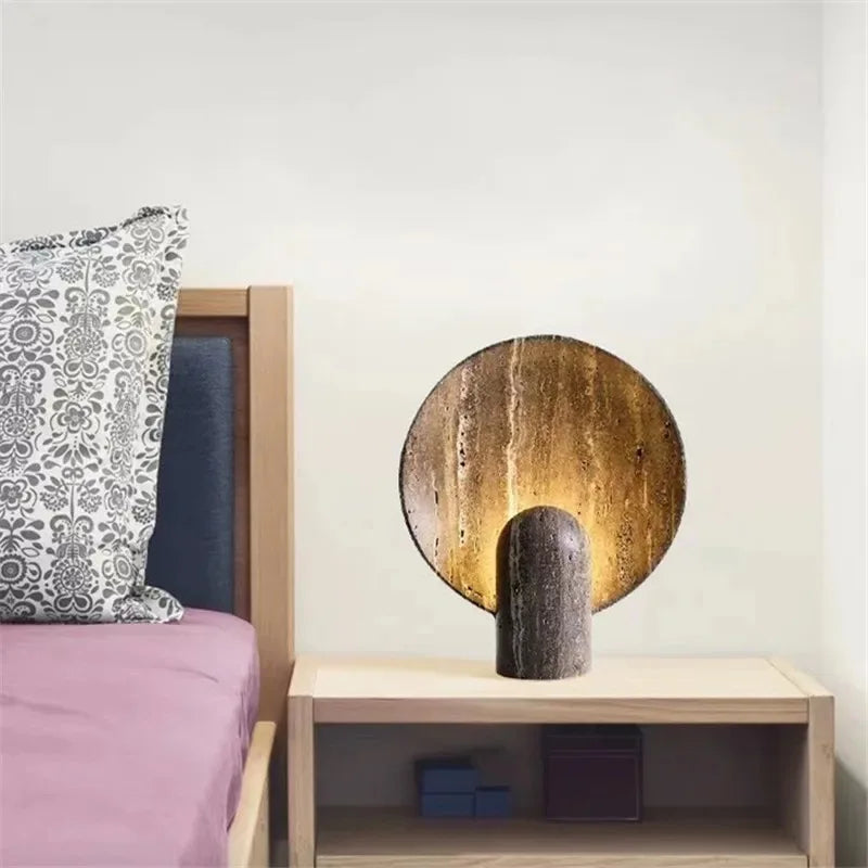 Warm radiance from the Jupiter Halo Table Lamp on a wooden nightstand, brown travertine with white veining and natural pitting delivering earthy grounded illumination, by Domus Collective.