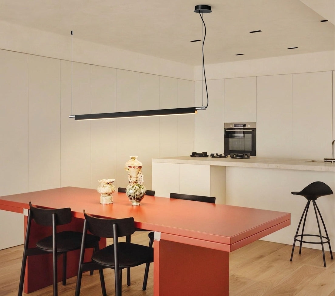 A Lama dell'Architetto Pendant Light by Domus Collective, in black. A minimalist linear pendant above a red dining table beside an open kitchen, defining the dining zone with clean architectural lines.