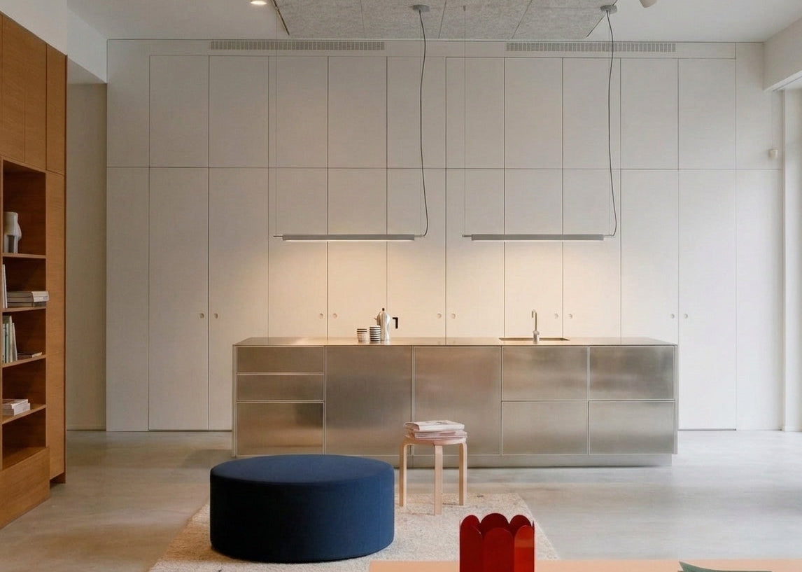 A Lama dell'Architetto Pendant Light by Domus Collective, in silver. A pair of linear pendant lights over a stainless steel kitchen island, giving even task lighting to the benchtop in a calm, minimalist kitchen.