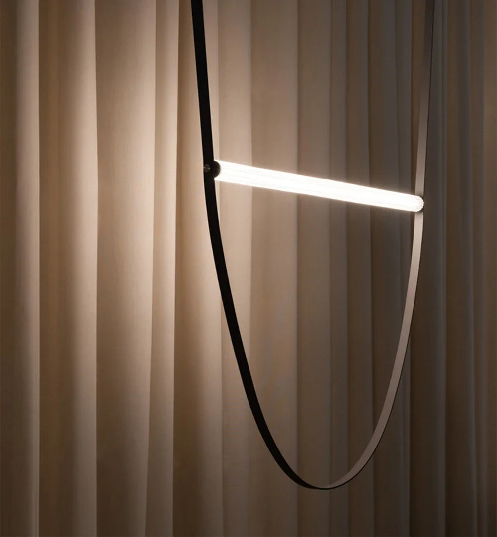 Black leather Leather Trapeze Suspension Light with single glowing LED bar against draped fabric backdrop, minimalist artisan pendant creating soft ambient illumination for intimate settings, by Domus Collective.