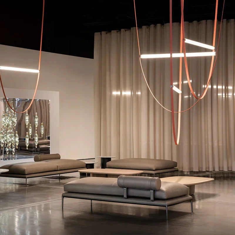 Dual Leather Trapeze Suspension Lights with terracotta and blush leather straps in luxury furniture showroom, curated sculptural pendants adding artistic ambiance to high-end commercial interiors, by Domus Collective.
