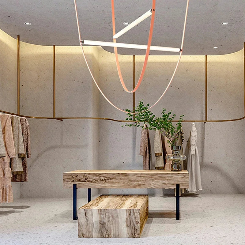 Leather Trapeze Suspension Light in blush and coral tones suspended above boutique retail display, handcrafted LED fixture bringing warmth and modern elegance to curated commercial spaces, by Domus Collective.