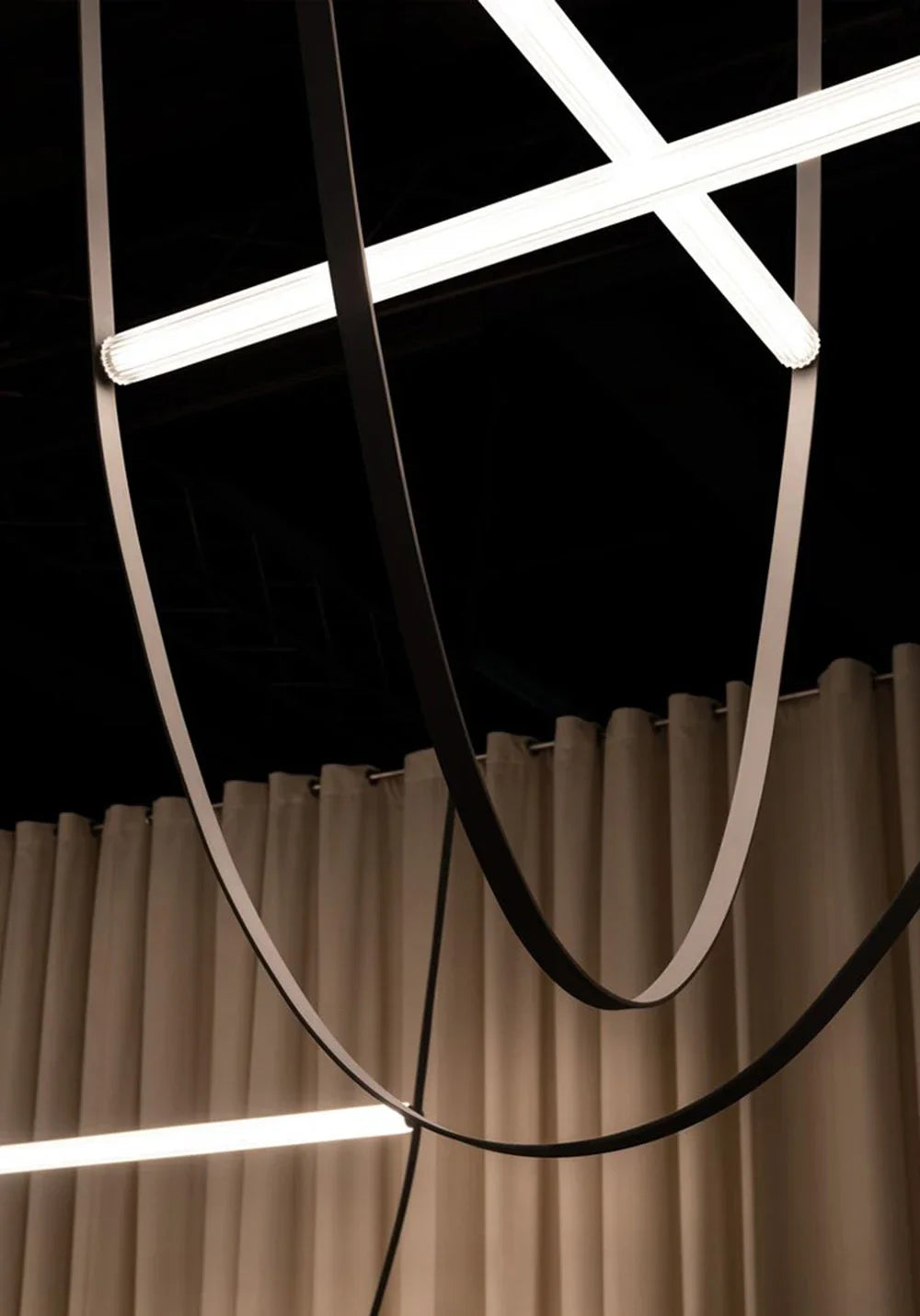 Leather Trapeze Suspension Lights with contrasting black and cream leather straps forming intersecting curves beneath crossed LED tubes, dramatic sculptural chandelier for avant-garde interiors, by Domus Collective.
