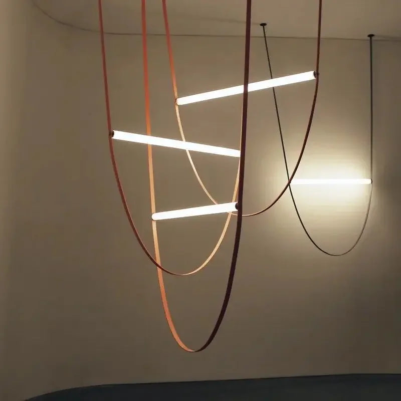 Leather Trapeze Suspension Lights with cascading terracotta and burgundy leather straps cradling illuminated LED tubes, sculptural artisan chandelier creating ambient warmth in contemporary interiors, by Domus Collective.