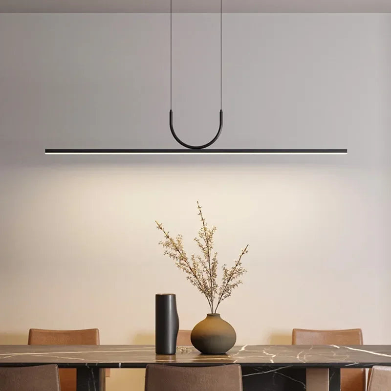 Linea Arc Pendant Light in matte black with sculptural curved suspension creating warm ambient glow over a contemporary marble dining table, Domus Collective curated lighting.