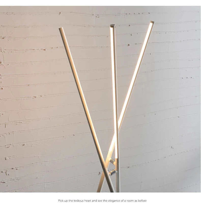 Close-up of the Linear Tension Floor Lamp in white finish showcasing three intersecting metal rods with integrated warm LED lighting, highlighting clean lines and balanced proportions against textured walls.