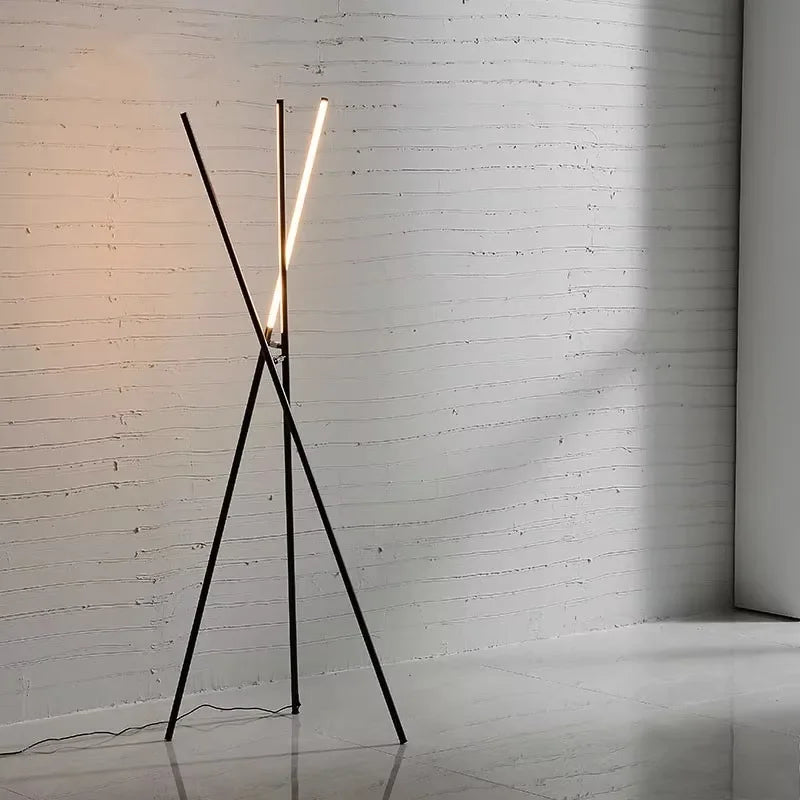 Linear Tension Floor Lamp in matte black metal finish with angular tripod base and illuminated LED bar, creating sculptural geometric drama against textured white brick walls, by Domus Collective.