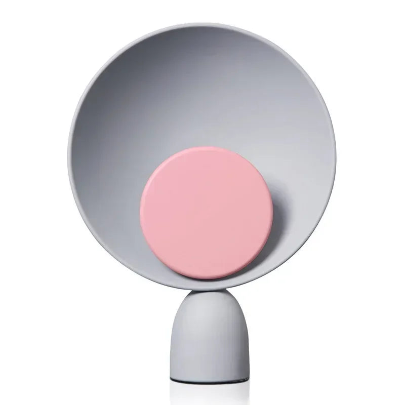 Lunar Eclipse Table Lamp featuring soft pink accent disc against grey circular reflector on matte iron base, its gentle feminine aesthetic ideal for modern bedrooms and living spaces, by Domus Collective.