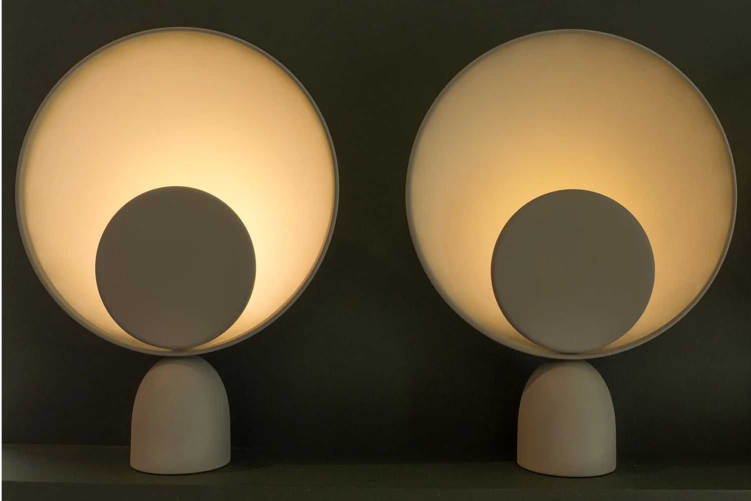 Pair of Lunar Eclipse Table Lamps with grey accent discs glowing warmly against a dark backdrop, their celestial-inspired forms delivering diffused ambient illumination for serene living spaces, by Domus Collective. 