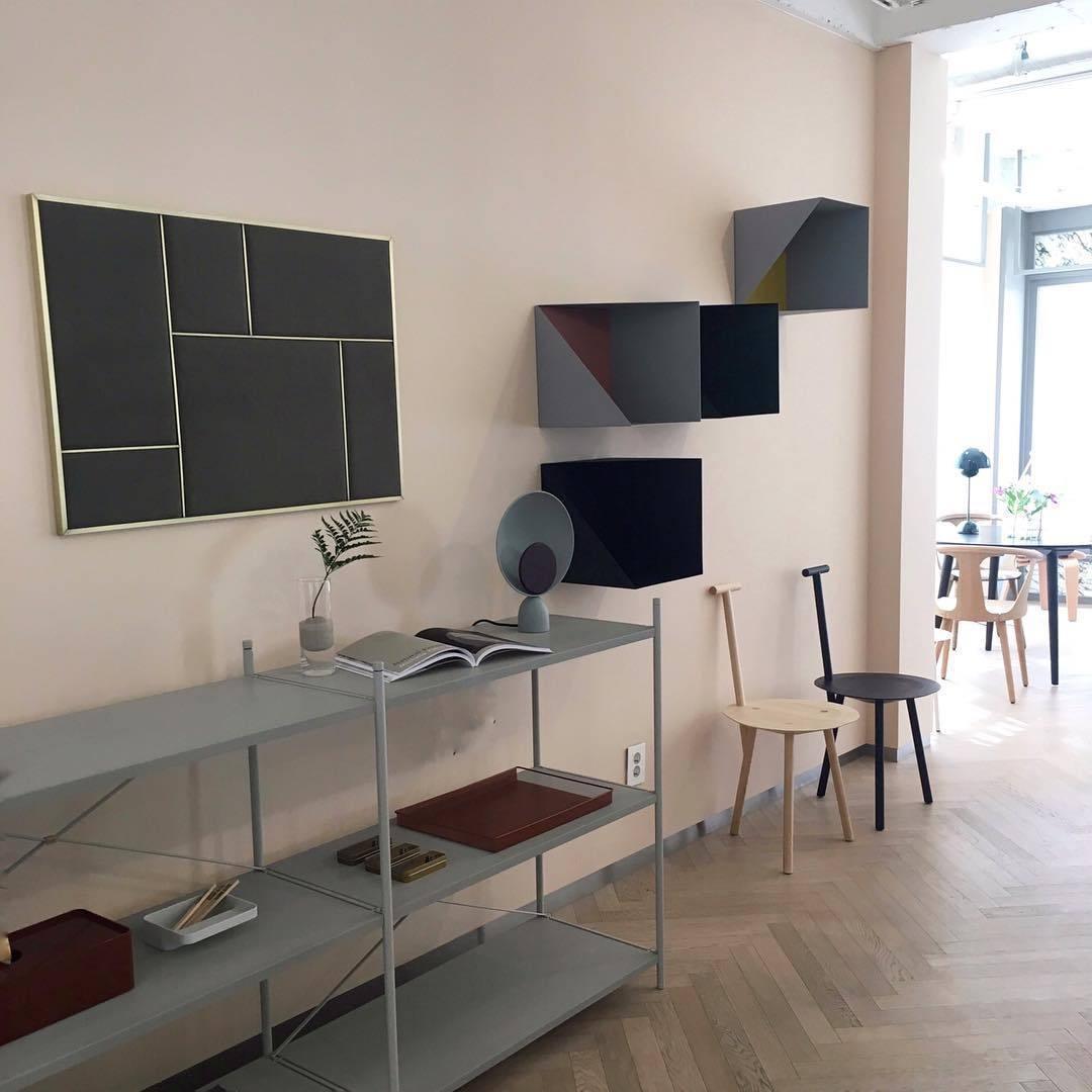 Lunar Eclipse Table Lamp in grey-purple with burgundy accent displayed on a minimalist metal shelving unit in a Scandinavian-inspired showroom with herringbone flooring, by Domus Collective.