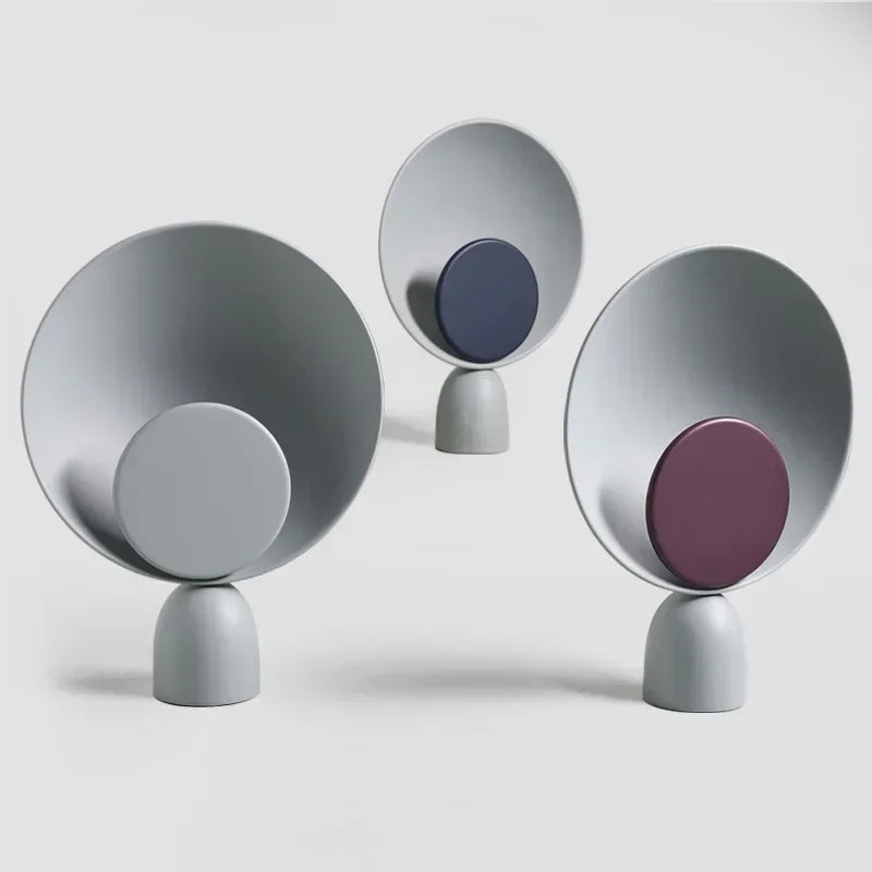 Three Lunar Eclipse Table Lamps showcasing grey, navy, and purple accent disc options on matte grey iron bases, their sculptural circular forms creating artistic focal points for modern interiors.