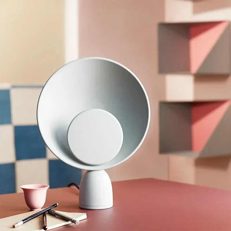 Lunar Eclipse Table Lamp with grey disc accent on a coral surface against a colorful geometric backdrop, demonstrating its versatile design for playful contemporary spaces, by Domus Collective.
