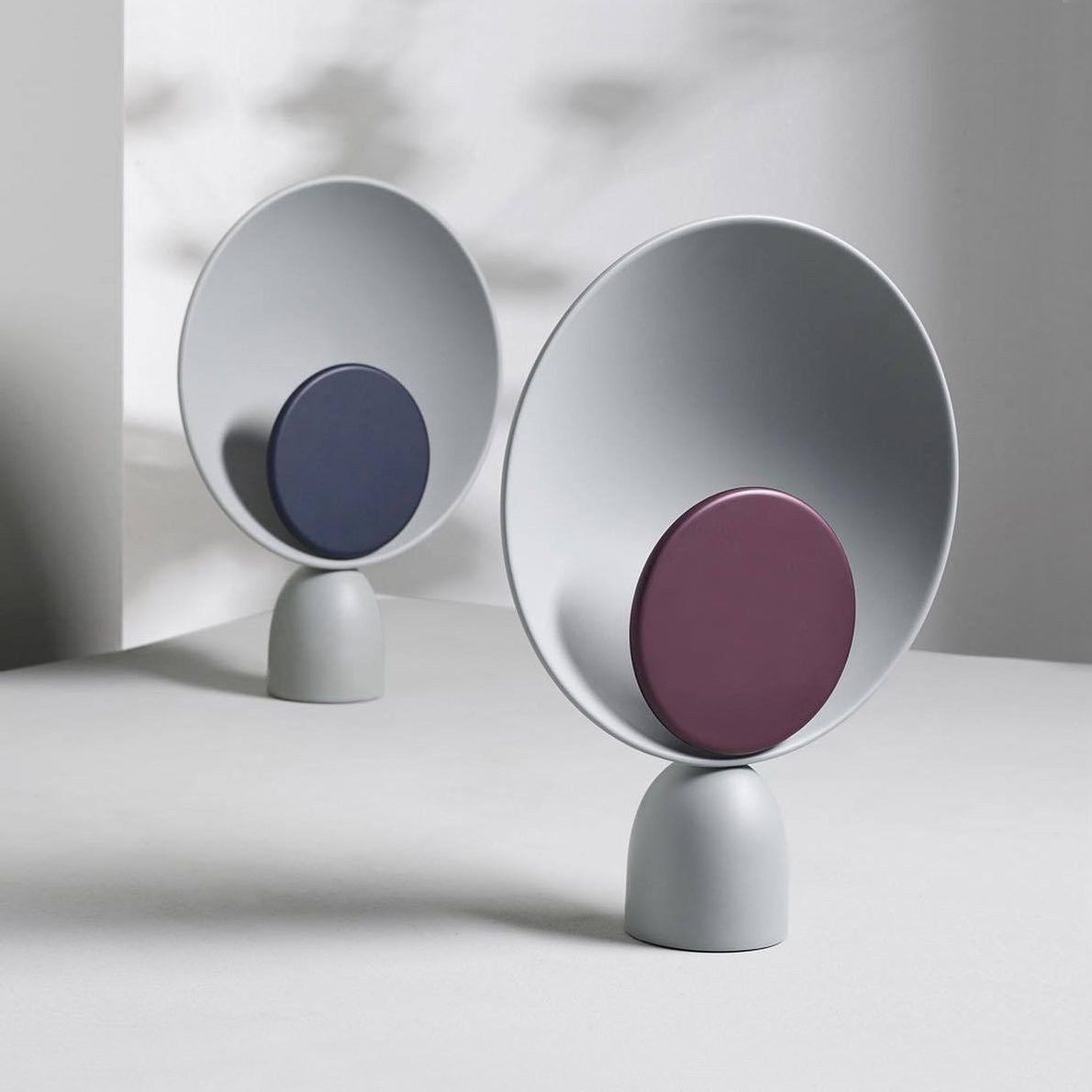 Pair of Lunar Eclipse Table Lamps in navy and purple accent finishes with soft grey bases, their elegant eclipse-inspired silhouettes casting gentle shadows in diffused natural light.