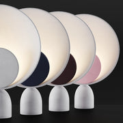 Lunar Eclipse Table Lamps displayed in four accent colors including grey, navy, burgundy, and pink discs against illuminated circular reflectors on sculptural grey iron bases, by Domus Collective.
