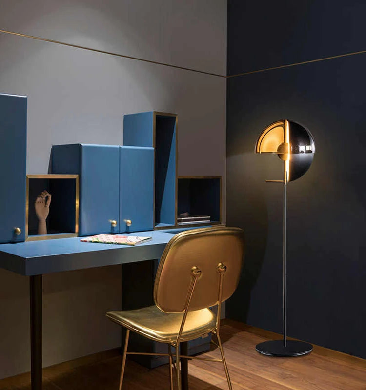 Lunar Visor Floor Lamp casting warm atmospheric light in a moody blue home office with gold accents, futuristic sculptural design by Domus Collective.