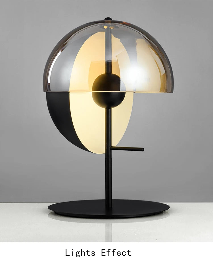 Lunar Visor Table Lamp illuminated, showcasing its spherical smoked glass shade with amber inner diffuser and central black orb detail on matte black base, contemporary lighting by Domus Collective.