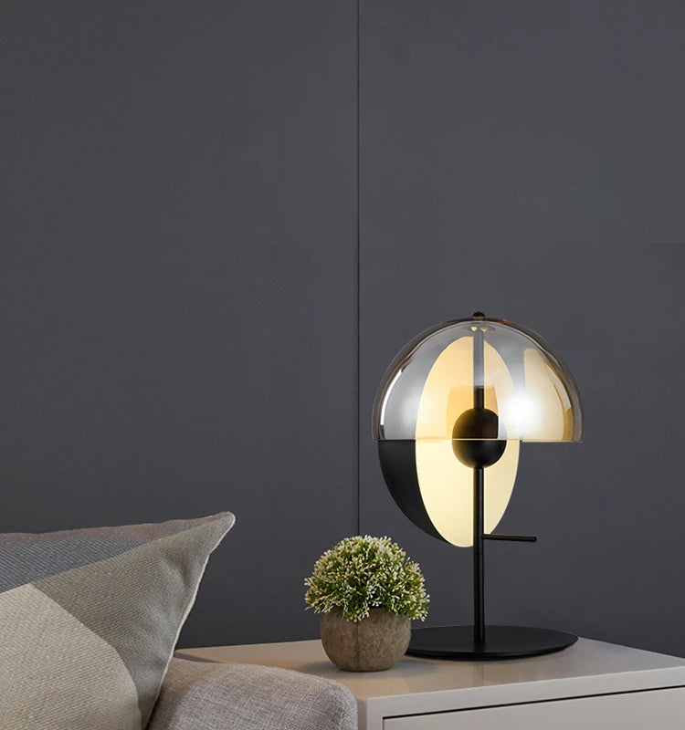 
Lunar Visor Table Lamp with smoked glass globe and warm amber diffuser creating soft atmospheric light against dark grey paneling, modern bedroom accent by Domus Collective.