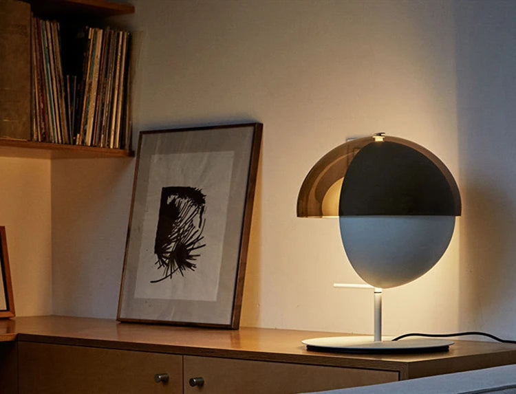 Lunar Visor Table Lamp with smoked glass dome and matte black visor accent casting warm ambient glow on a mid-century credenza, sculptural designer lighting by Domus Collective.