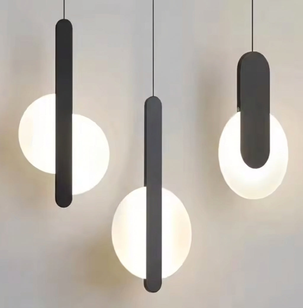 Three matte black Matchstick Slice Pendant Lights suspended above a kitchen island, their frosted globes creating soft, layered illumination for sophisticated modern dining, by Domus Collective.