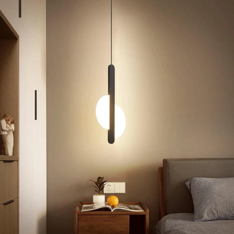 Warm ambient glow from the Matchstick Slice Pendant Light, its frosted glass orb and matte black stem bringing refined minimalism to cozy bedside moments, by Domus Collective.